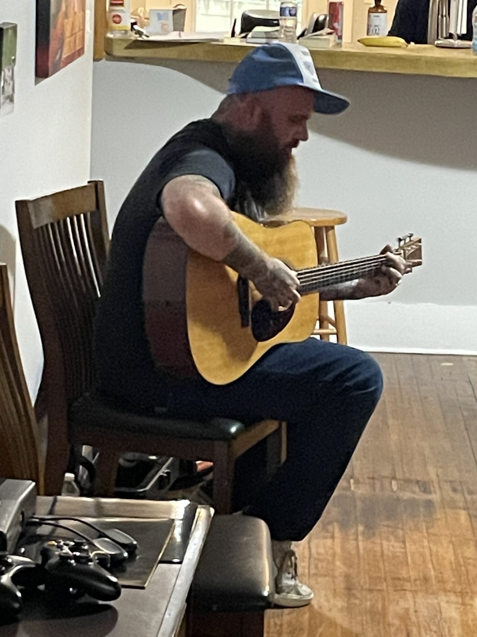 Musician seated, playing guitar in cozy venue.