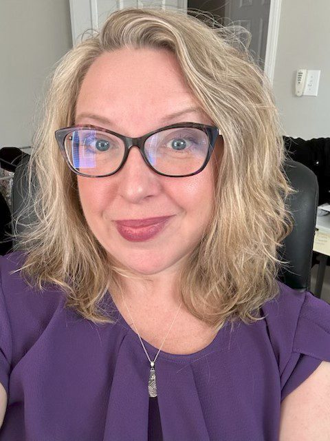 Smiling woman with glasses in purple top.